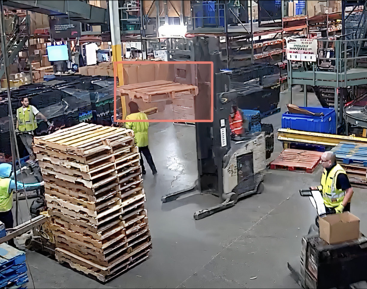 Real-time AI monitoring in a manufacturing facility with orange bounding boxes identifying workers using a lift for hazard detection.