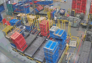 High-angle view of an automated warehouse floor featuring organized stacks of blue and red pallets and conveyor systems.